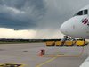 Am Flughafen Stuttgart steht ein Flugzeug. Ein weiteres ist im Landeanflug vor dunklen Gewitterwolken.